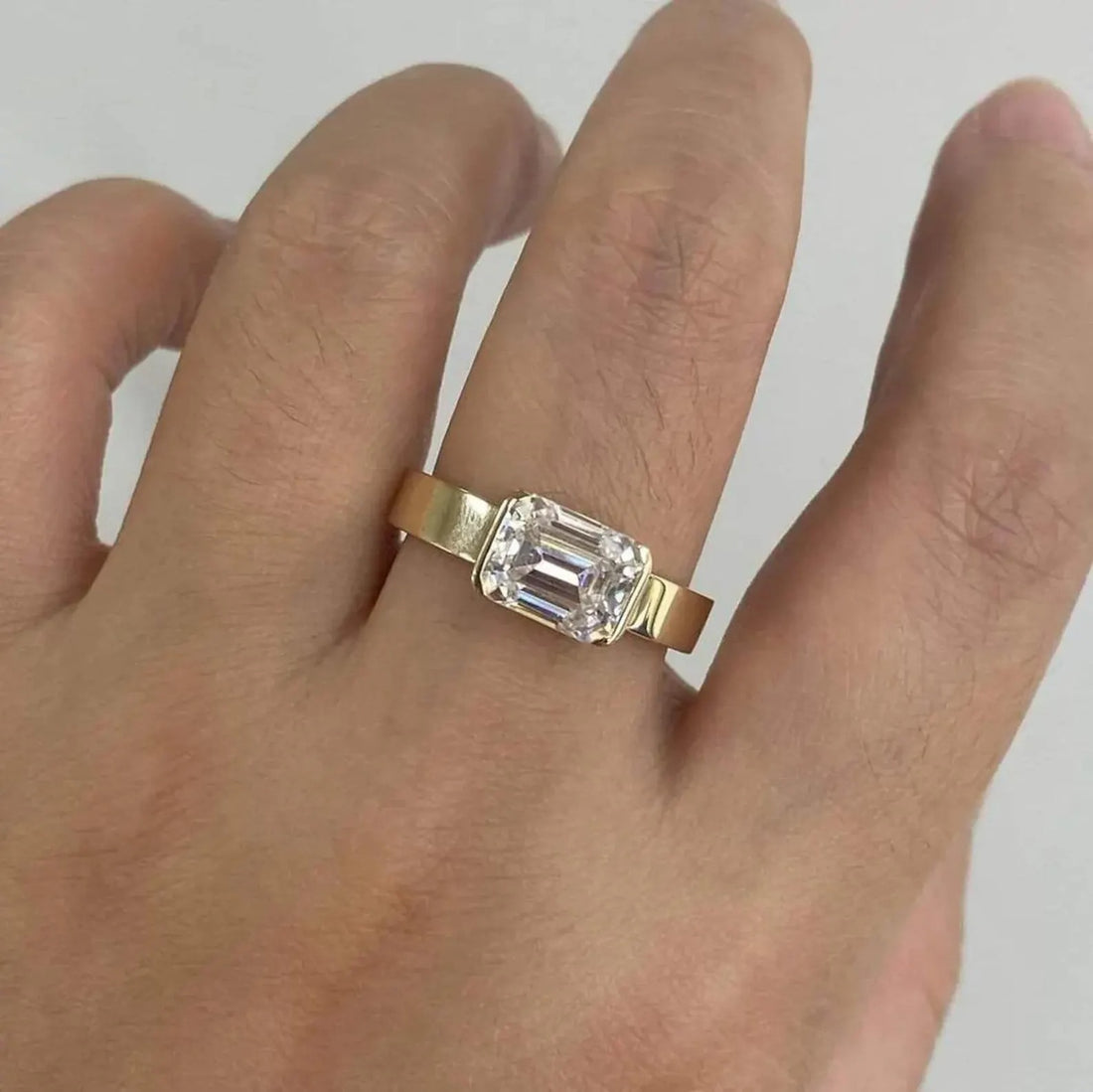 East west emerald cut lab grown diamond engagement ring on a wide yellow gold band