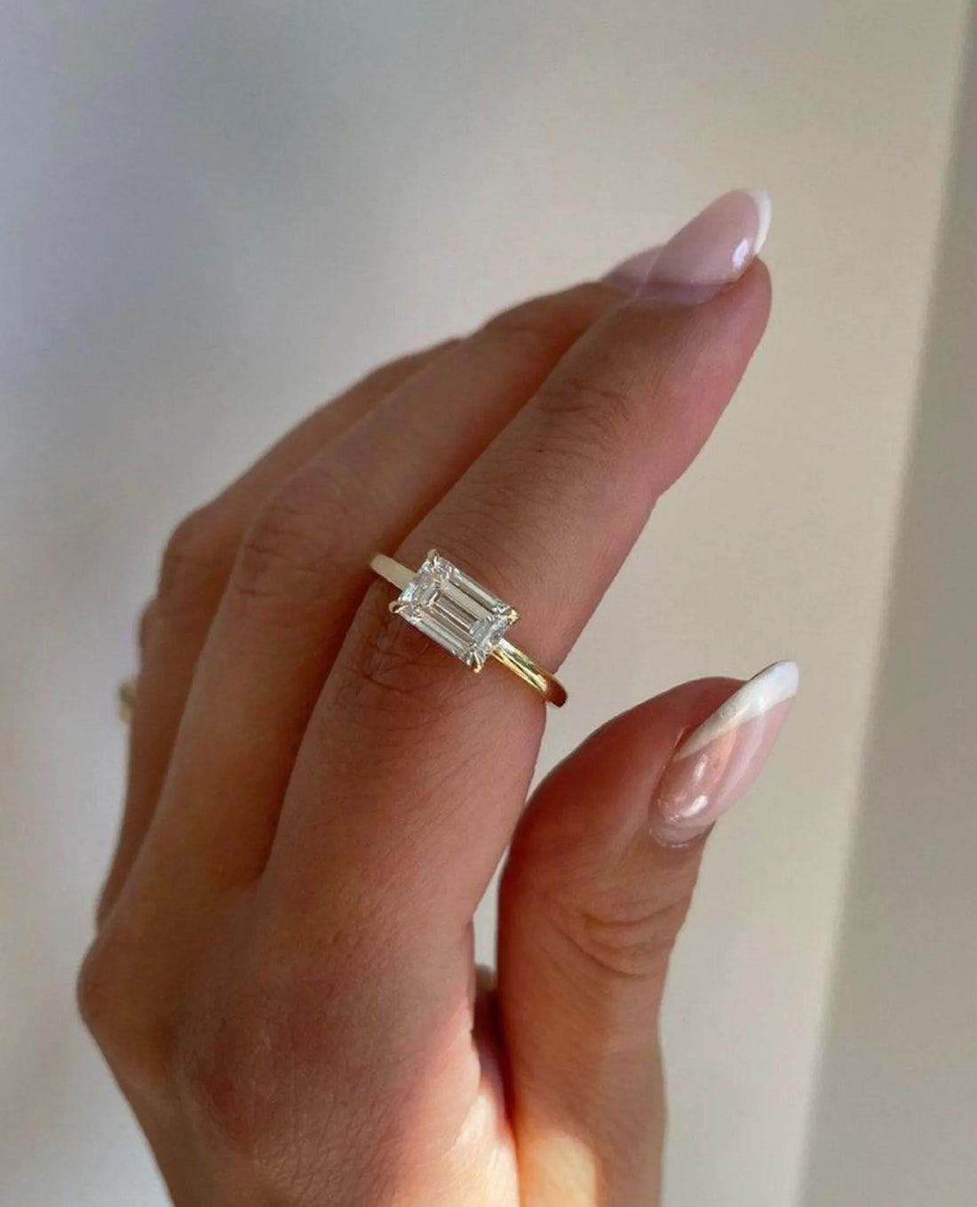 East west emerald cut lab grown diamond engagement ring on a slim yellow gold band