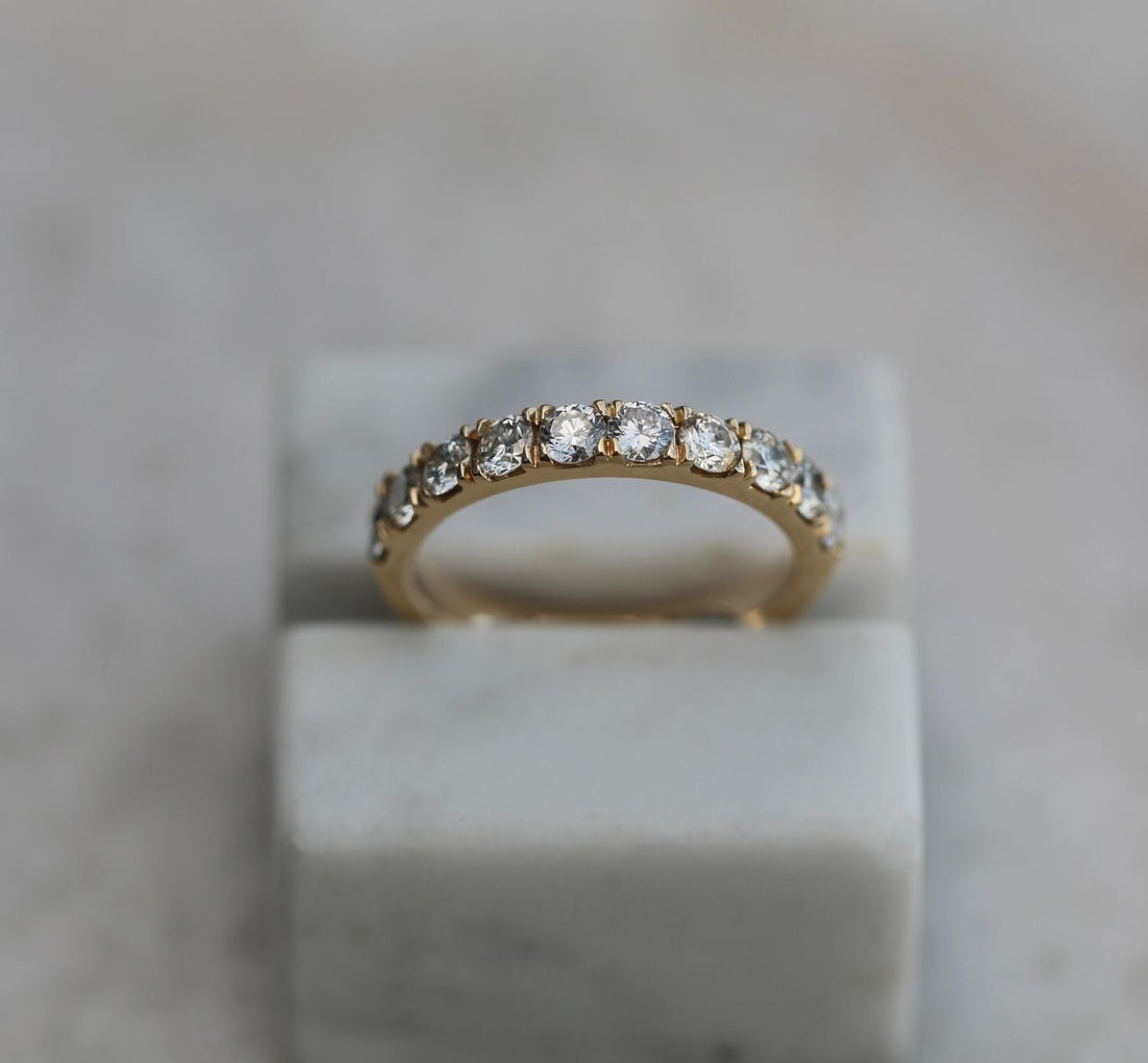 Round shared prong half eternity lab grown diamond wedding band in yellow gold on a marble block, front view