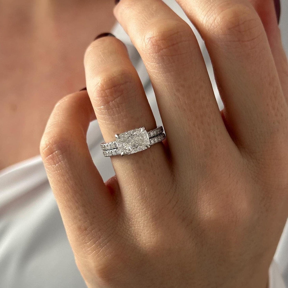 East-west elongated cushion moissanite bridal set with pave band in white gold worn on the hand