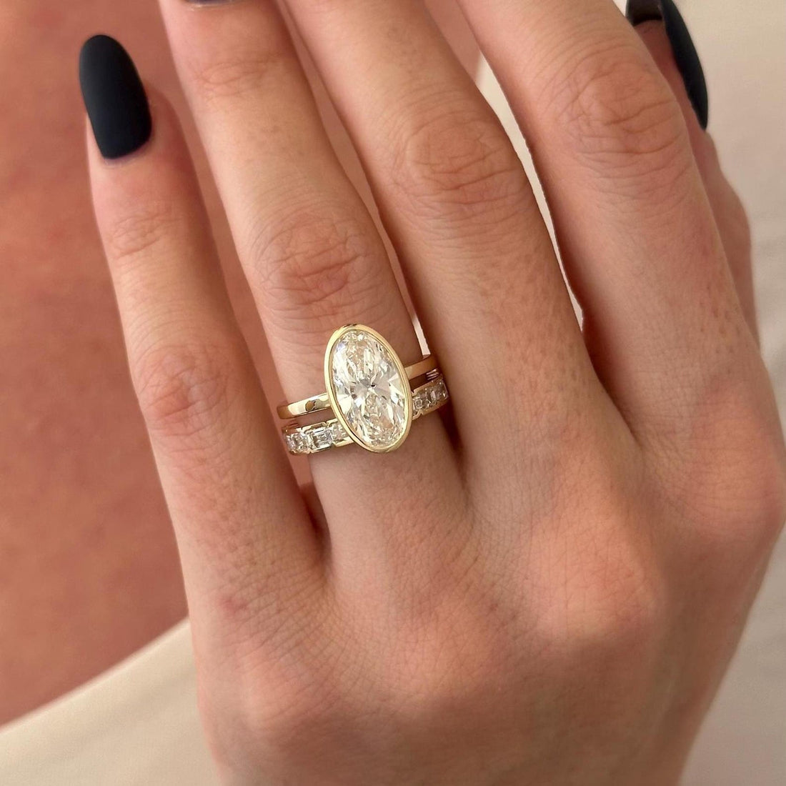 Elongated oval lab grown diamond bezel bridal set with emerald cut stone band in yellow gold on the hand