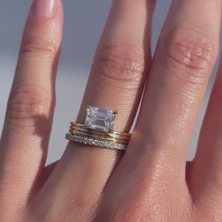 East-west emerald cut lab grown diamond solitaire on a ridged gold shank with pave band on the hand