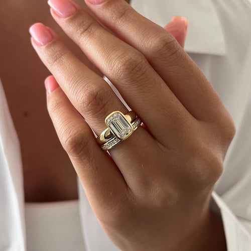 Emerald cut moissanite full bezel bridal set in yellow gold worn on the hand
