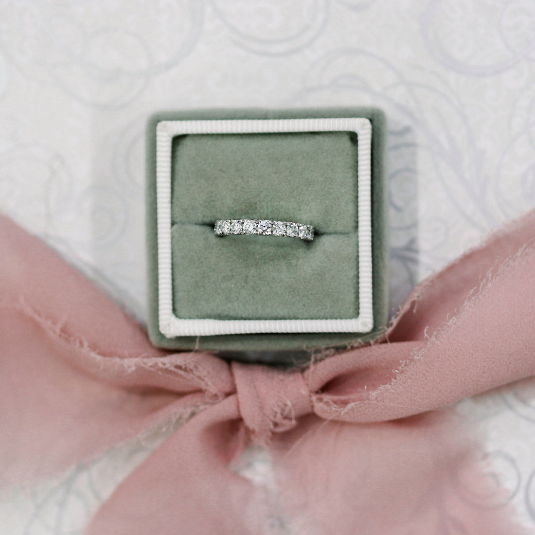 White gold scallop pave moissanite band in a green ring box with a pink ribbon