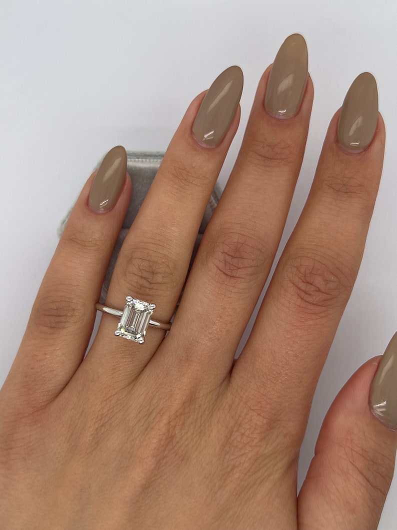 Emerald cut lab grown diamond claw solitaire ring in white metal on a slim band