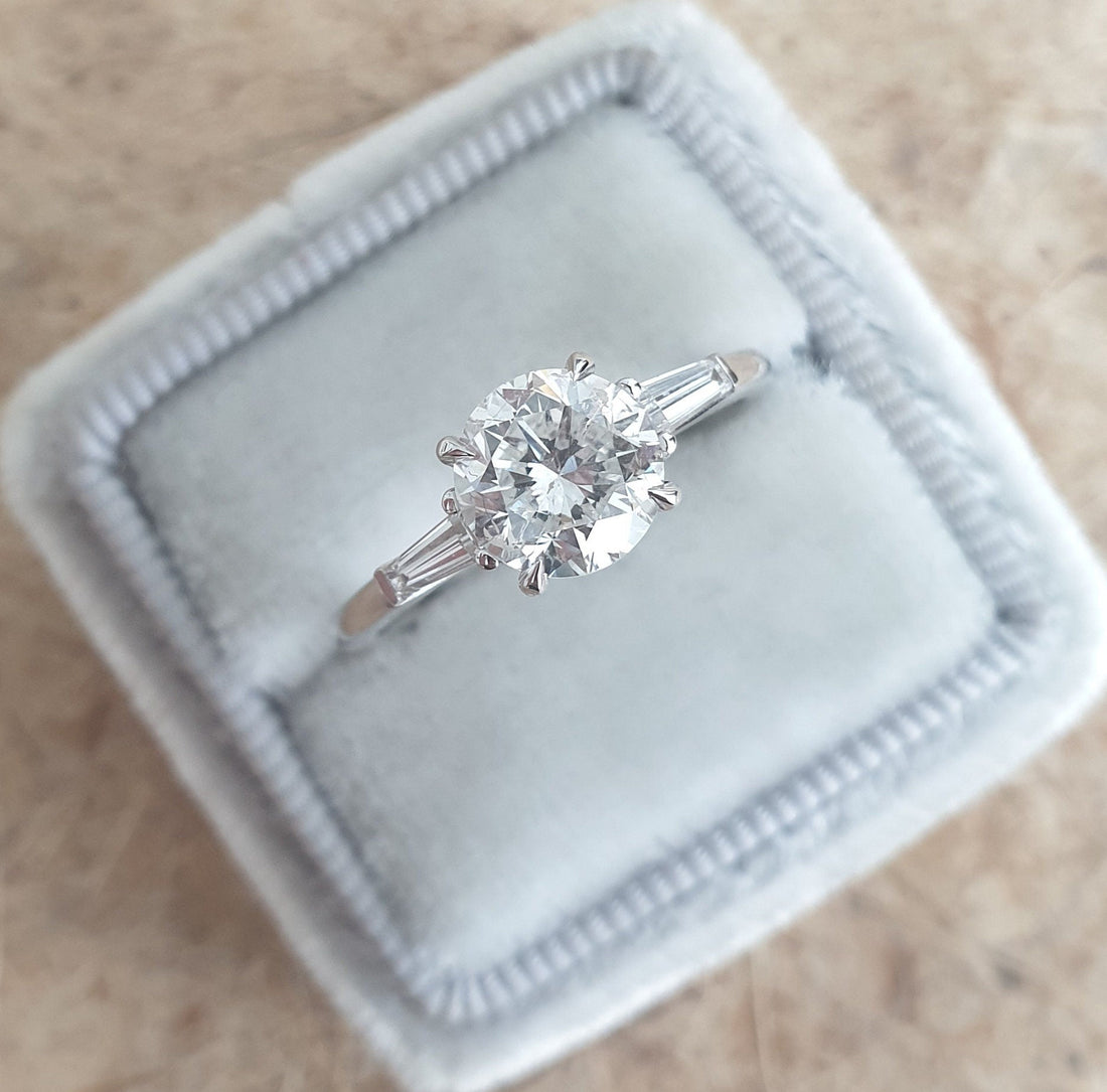 Round cut lab grown diamond three stone ring with tapered baguette sides in white metal