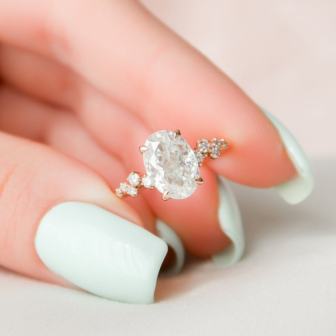 Oval cut moissanite cascading cluster engagement ring in rose gold held in hand