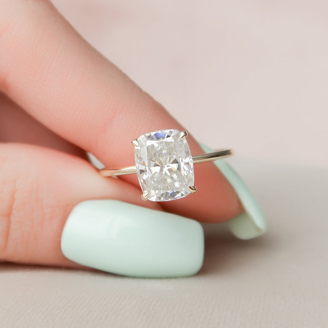 Elongated cushion cut moissanite thin band engagement ring in yellow gold held in hand