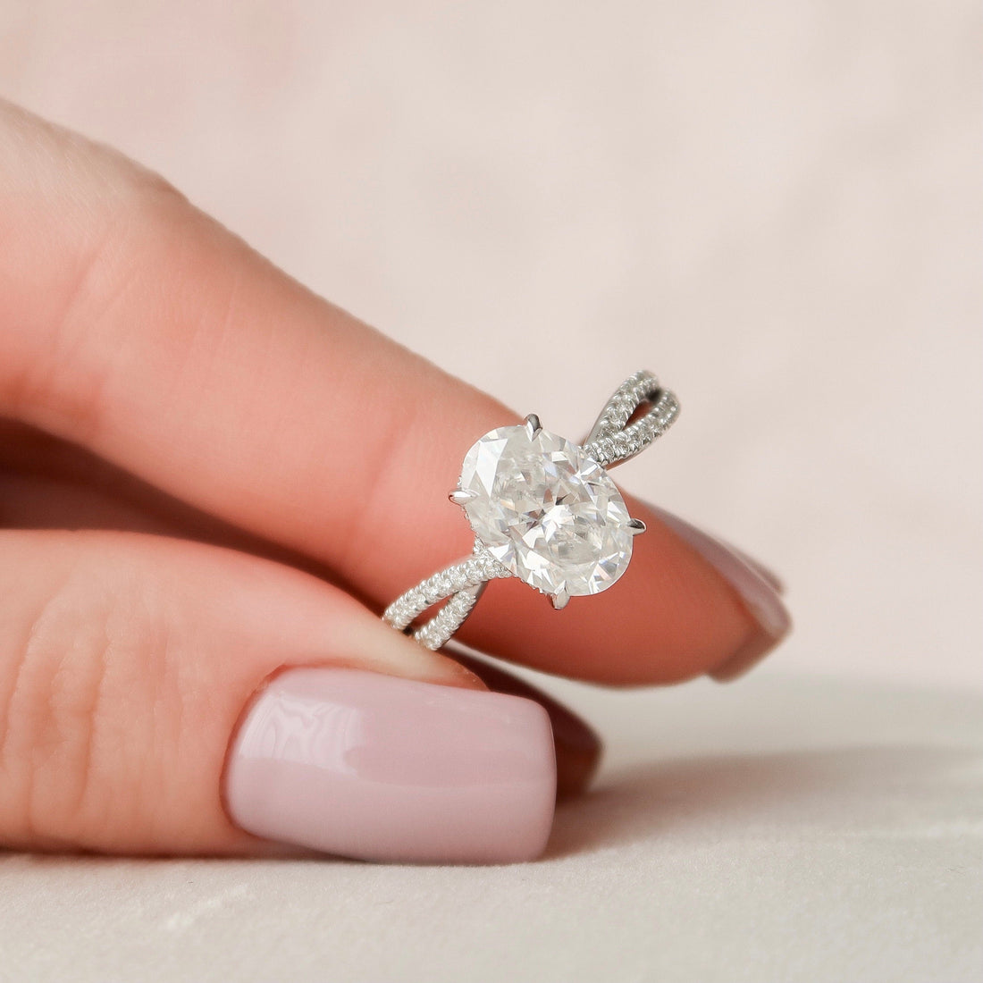 Oval cut moissanite hidden halo split shank engagement ring in white gold held in hand