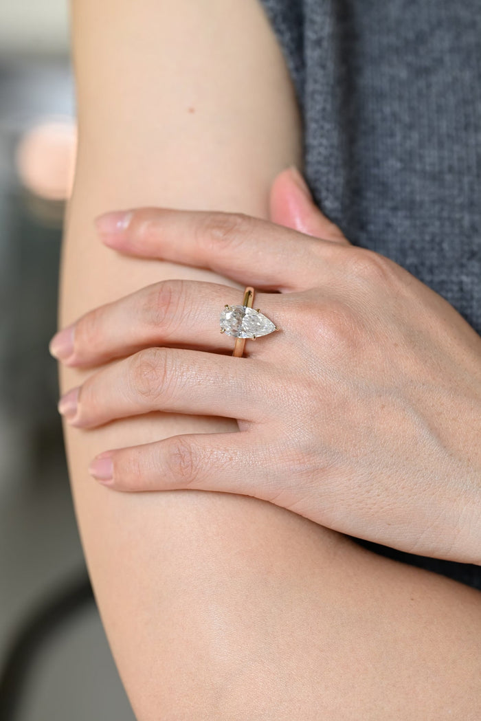 Elongated pear shaped moissanite statement solitaire engagement ring held by five slim claws on a smooth polished yellow gold band, view 2