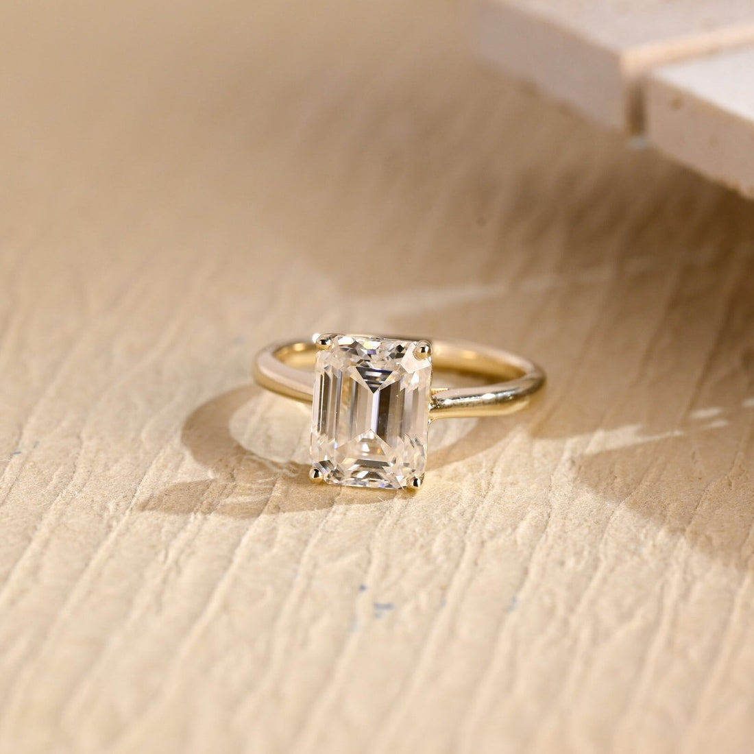 Emerald cut moissanite solitaire engagement ring in four claws above a scrolled open gallery on a slim yellow gold band