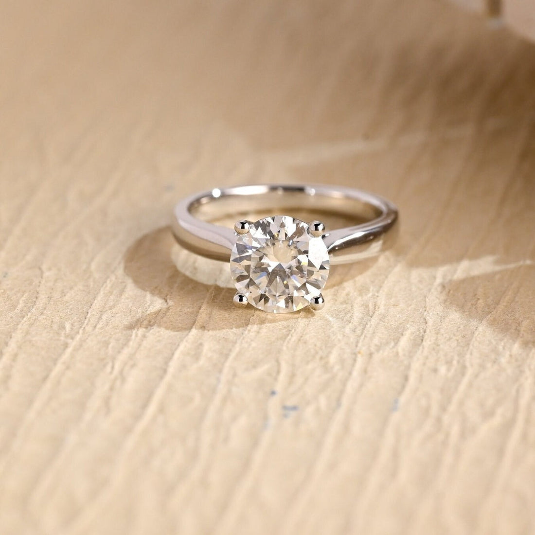 Round moissanite cathedral solitaire engagement ring held by four claws on a polished white gold band that sweeps up to the stone