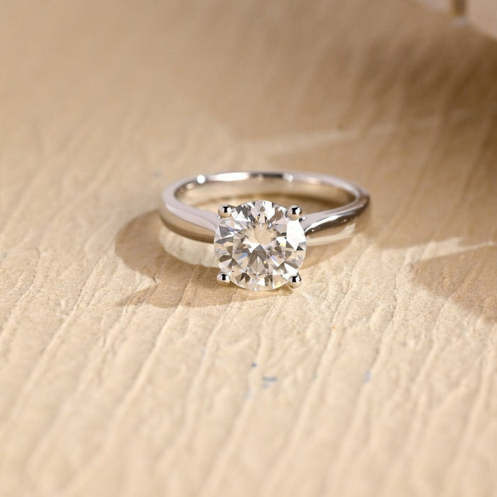 Round moissanite cathedral solitaire engagement ring held by four claws on a polished white gold band that sweeps up to the stone