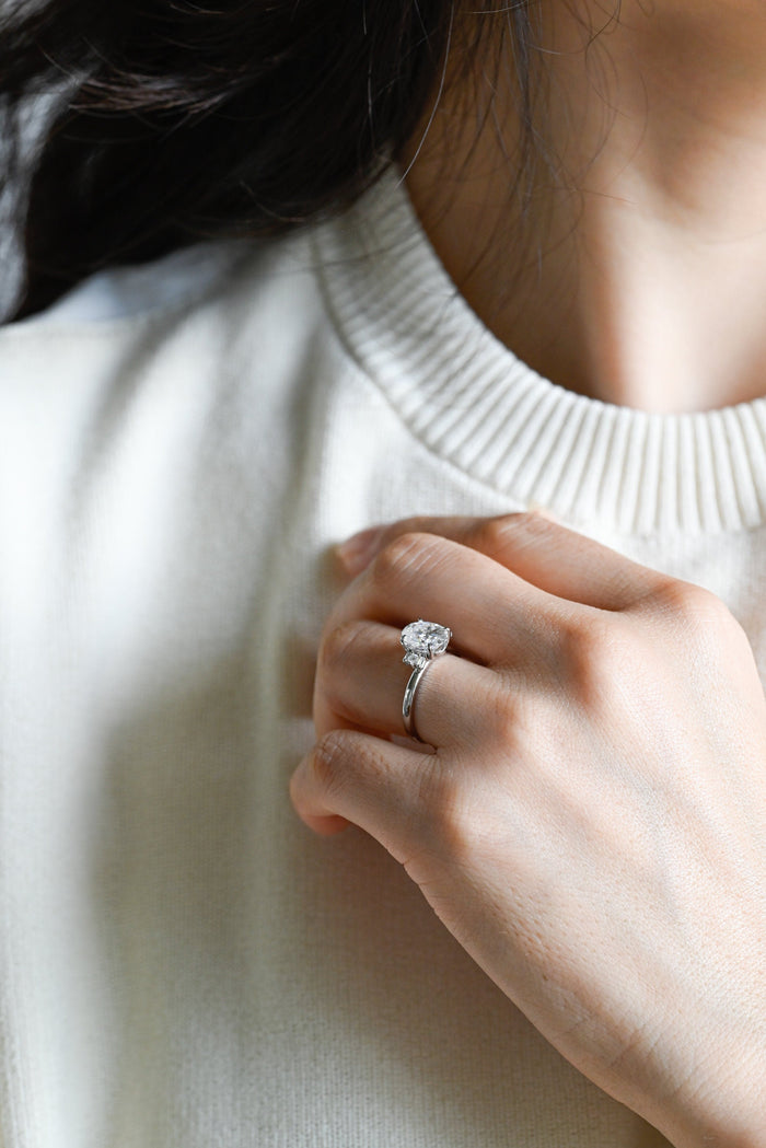 Oval moissanite engagement ring with two baguette stones and a round stone stacked on each side of the oval on a plain polished white gold band, view 2