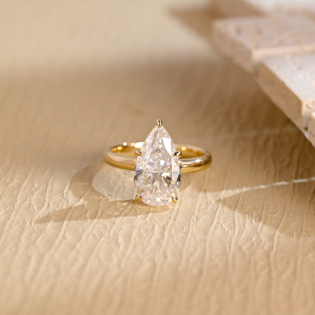 Elongated pear cut moissanite hidden halo engagement ring in six claws on a plain polished yellow gold band