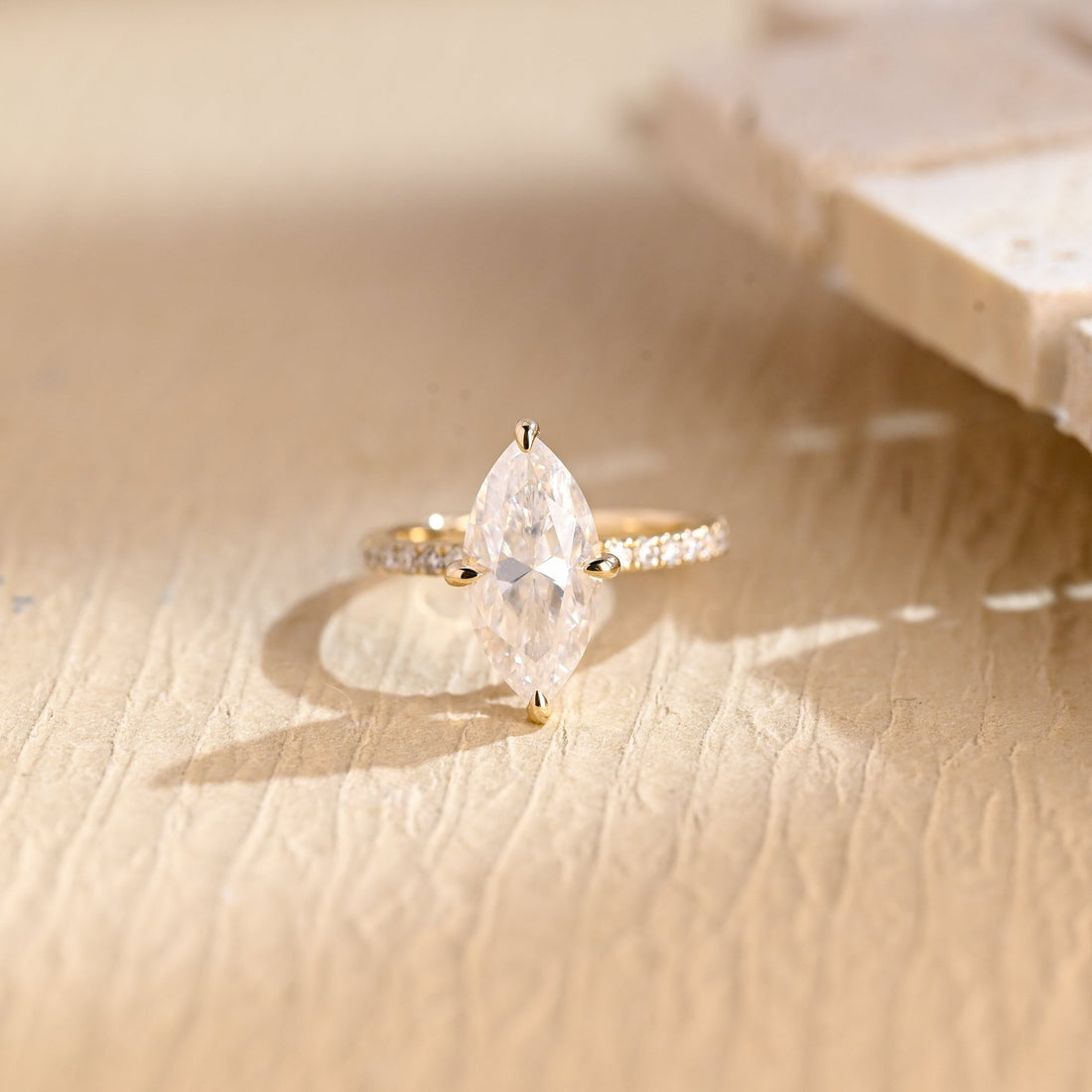 Four claw marquise cut moissanite solitaire engagement ring on a pave set yellow gold band