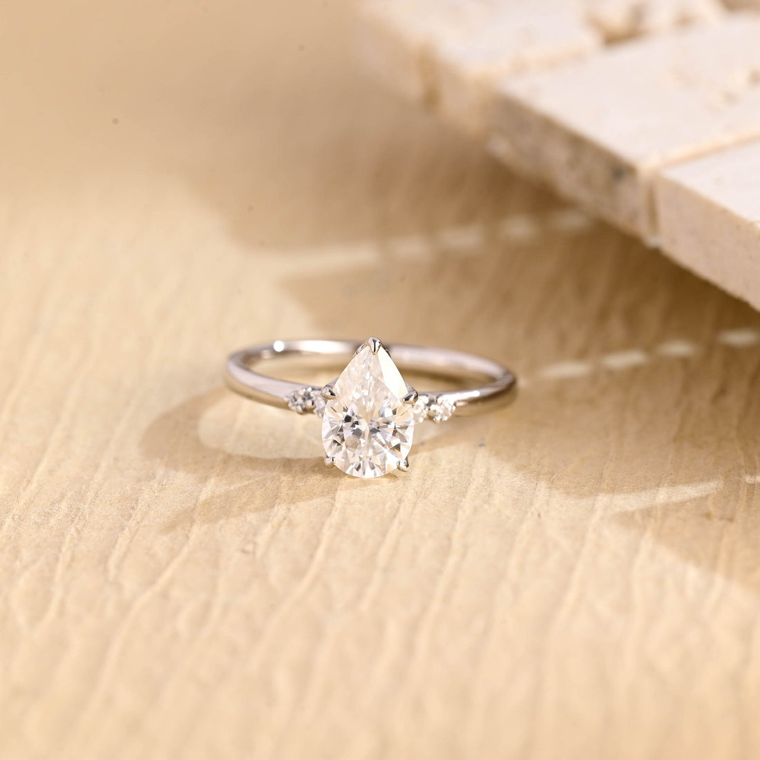 Pear cut moissanite five stone engagement ring with two small round stones on each shoulder of a slim polished white gold band