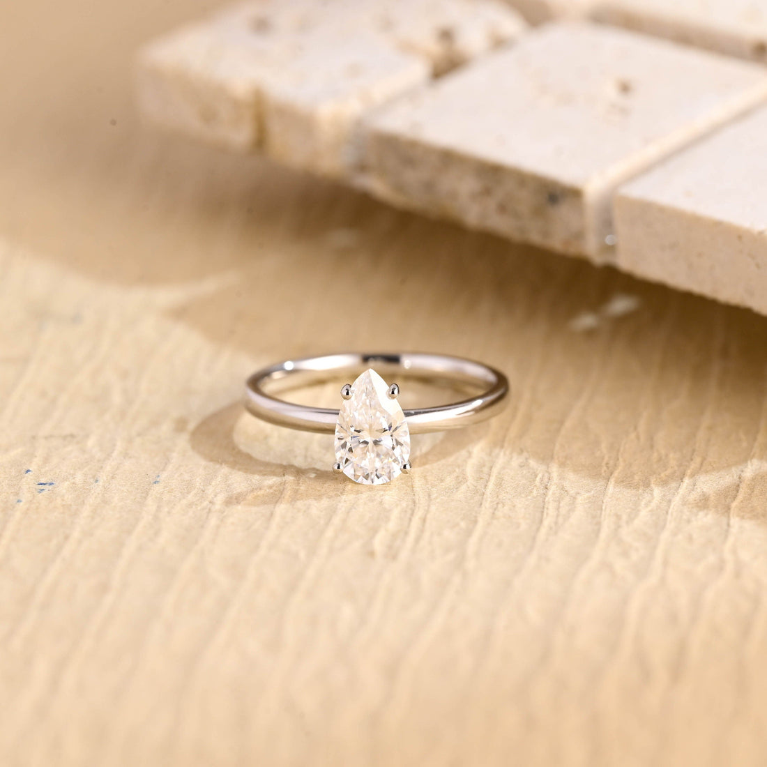 Delicate pear cut moissanite solitaire engagement ring in four small claws on a slim plain polished white gold band