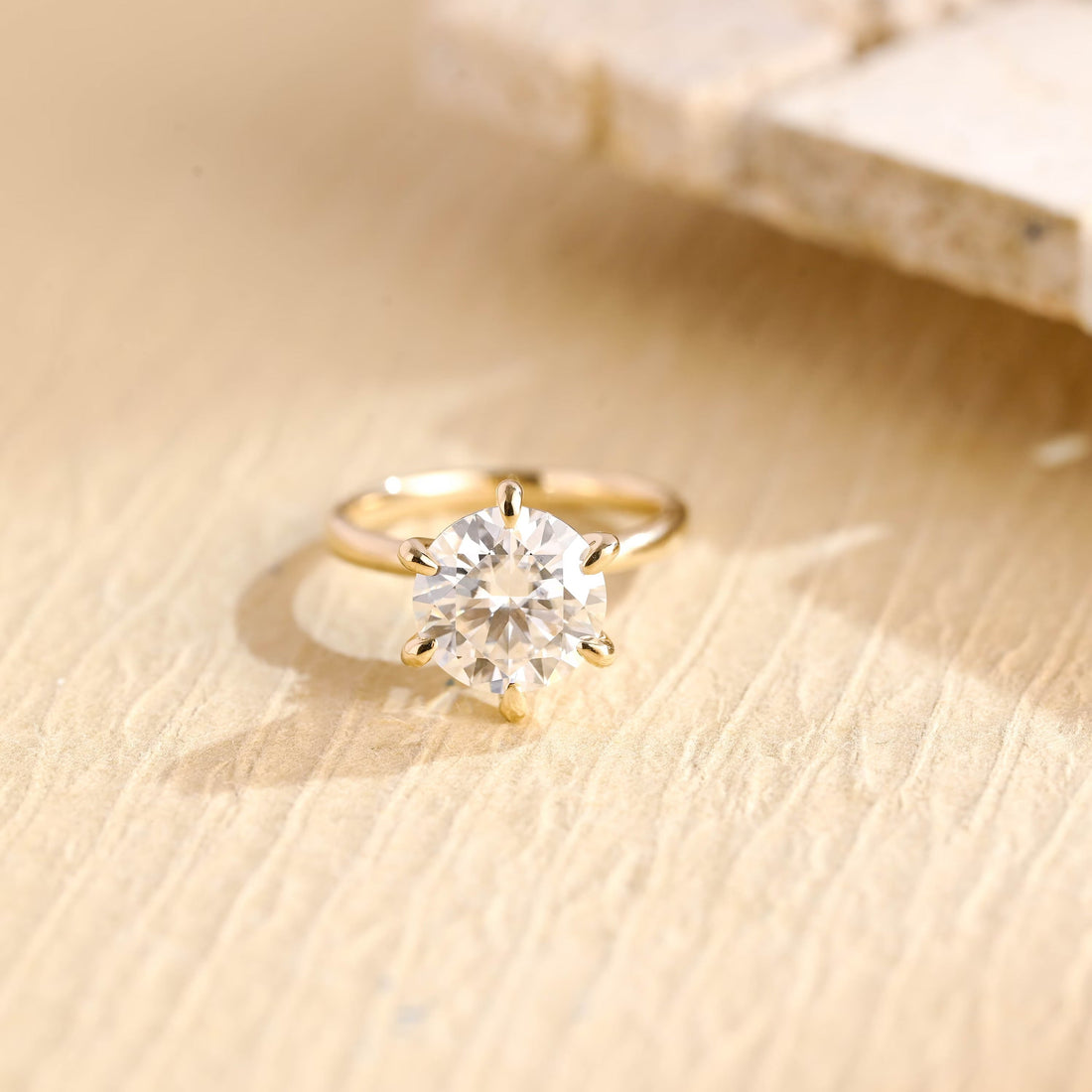 Round moissanite six claw solitaire engagement ring with teardrop shaped claws on a fine smooth yellow gold band