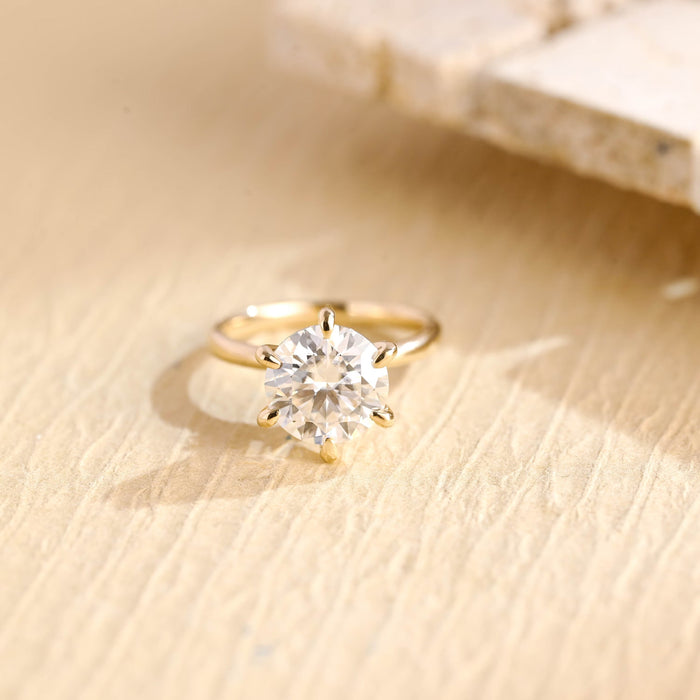 Round moissanite six claw solitaire engagement ring with teardrop shaped claws on a fine smooth yellow gold band