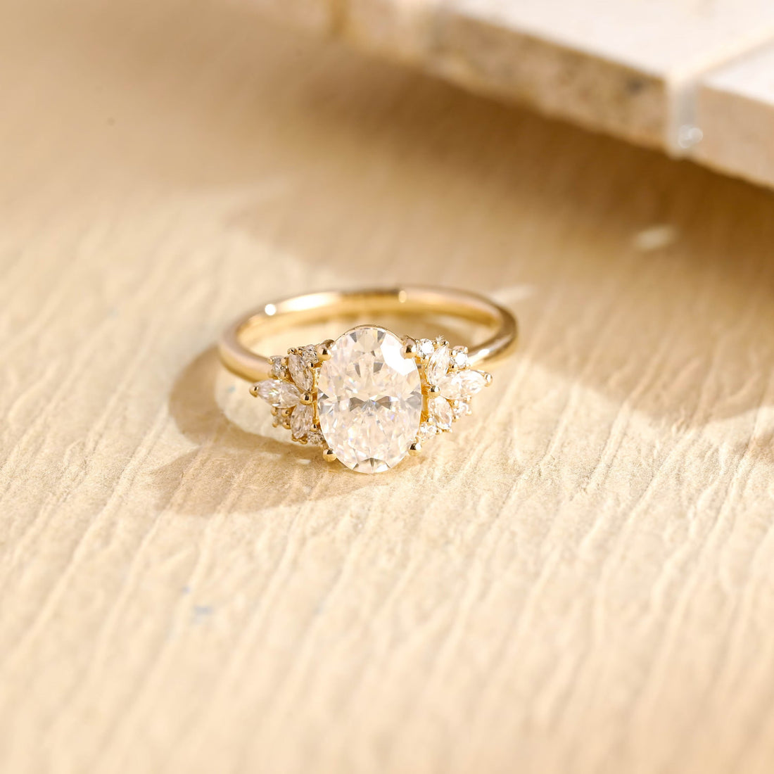 Oval moissanite engagement ring with a fan of marquise and small round stones on each side of the oval on a slim plain yellow gold band