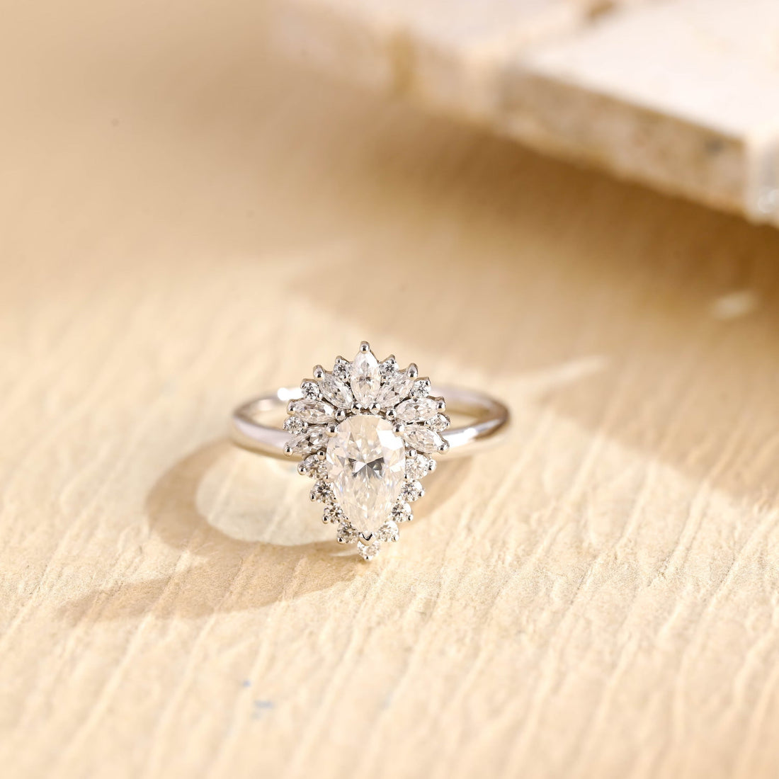 Pear cut moissanite cluster engagement ring with a halo of round stones and a fan of marquise stones above the centre stone on a slim polished white gold band