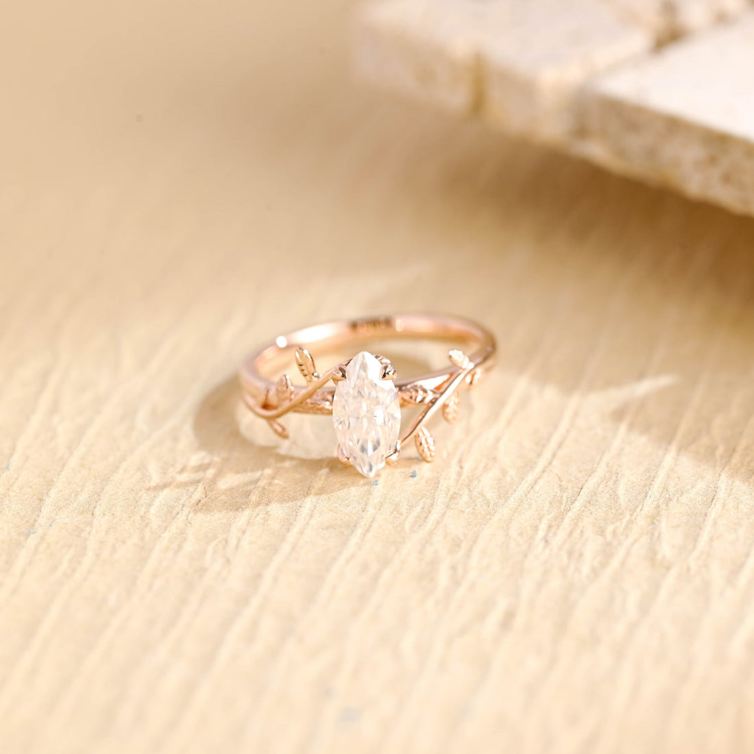 Marquise cut moissanite engagement ring on a rose gold band of twisting vines with small textured leaves
