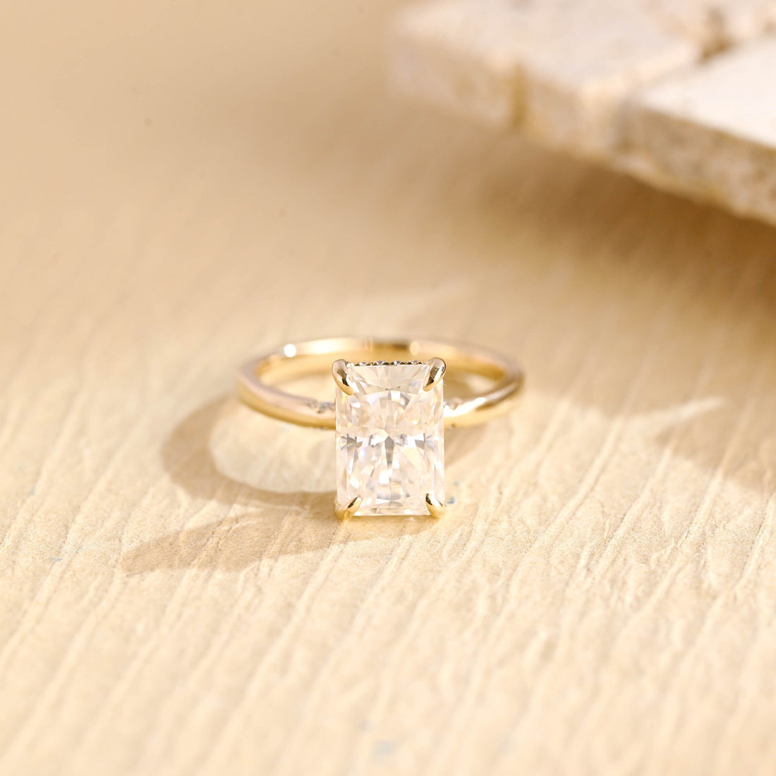 Elongated radiant cut moissanite hidden halo engagement ring in four claws on a polished yellow gold band with small flush set shoulder stones