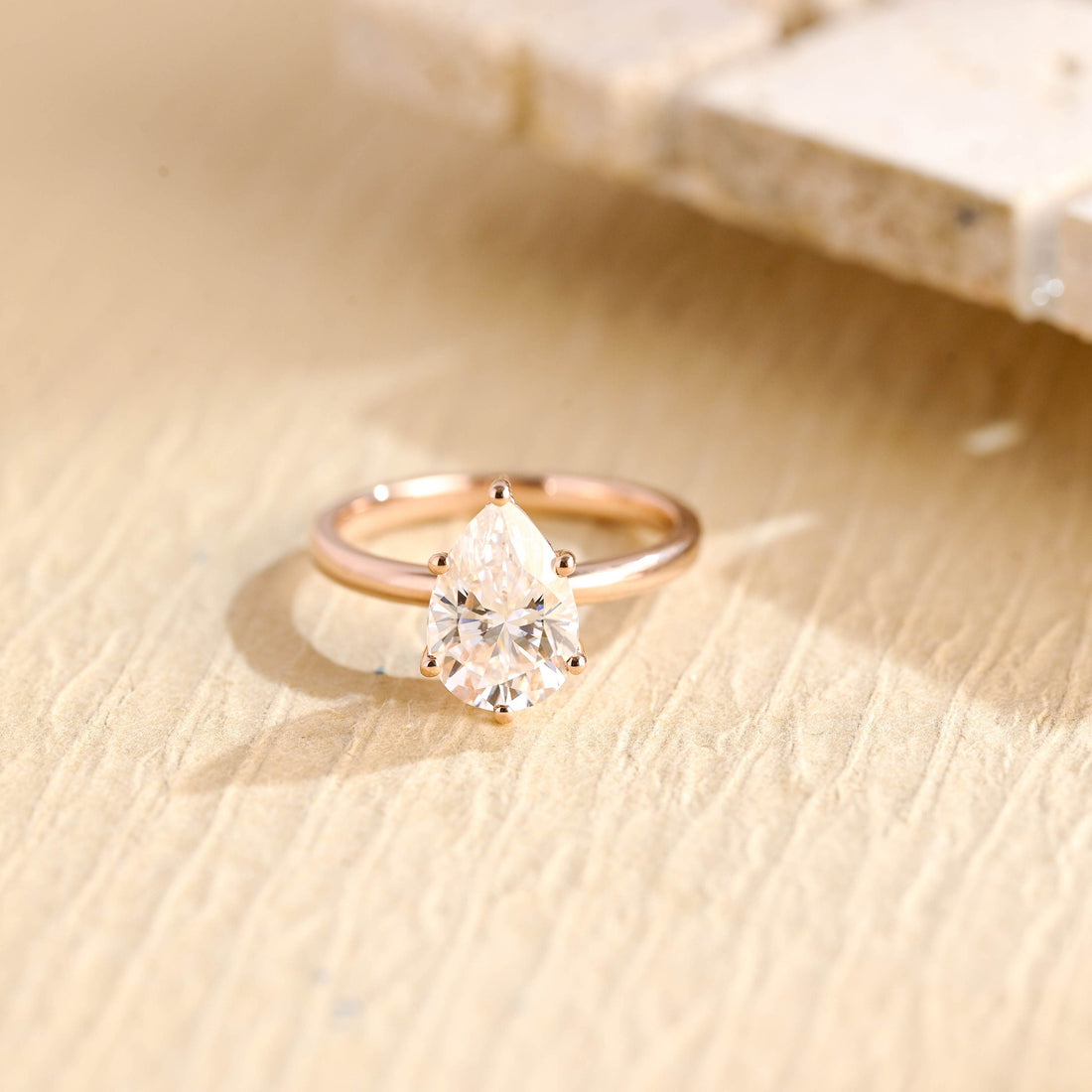 Pear cut moissanite solitaire engagement ring held in six claws on a plain polished rose gold band