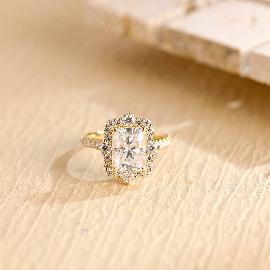 Radiant cut moissanite halo engagement ring with four larger round accent stones around the halo and a pave set yellow gold band