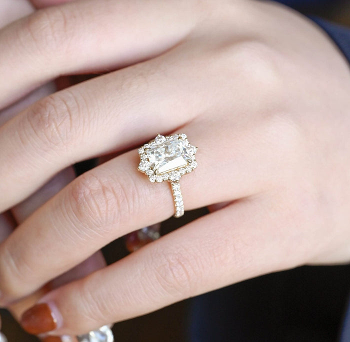 Radiant cut moissanite halo engagement ring with four larger round accent stones around the halo and a pave set yellow gold band, view 2