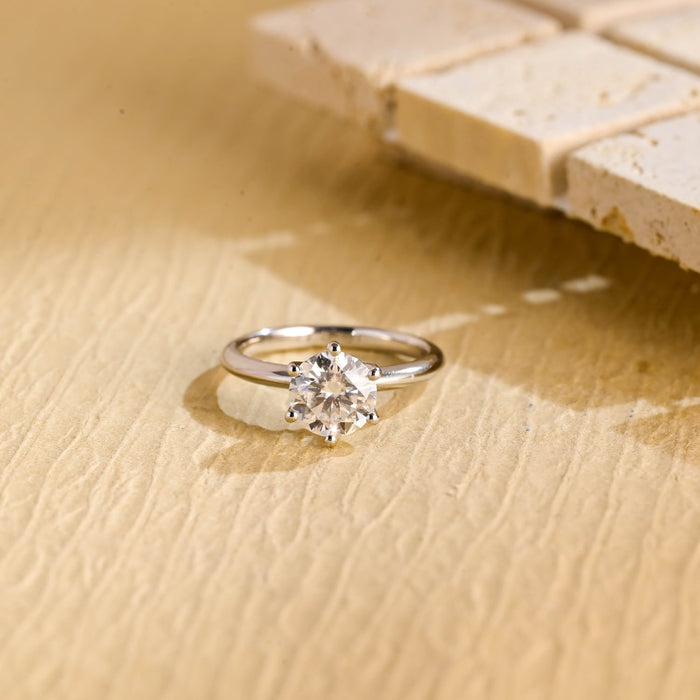 Round moissanite six prong solitaire engagement ring with button tipped prongs on a tapered rounded white gold band