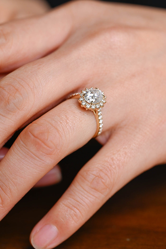 Oval moissanite sunburst halo engagement ring with pointed prong tips around the halo and a pave set yellow gold band, view 2