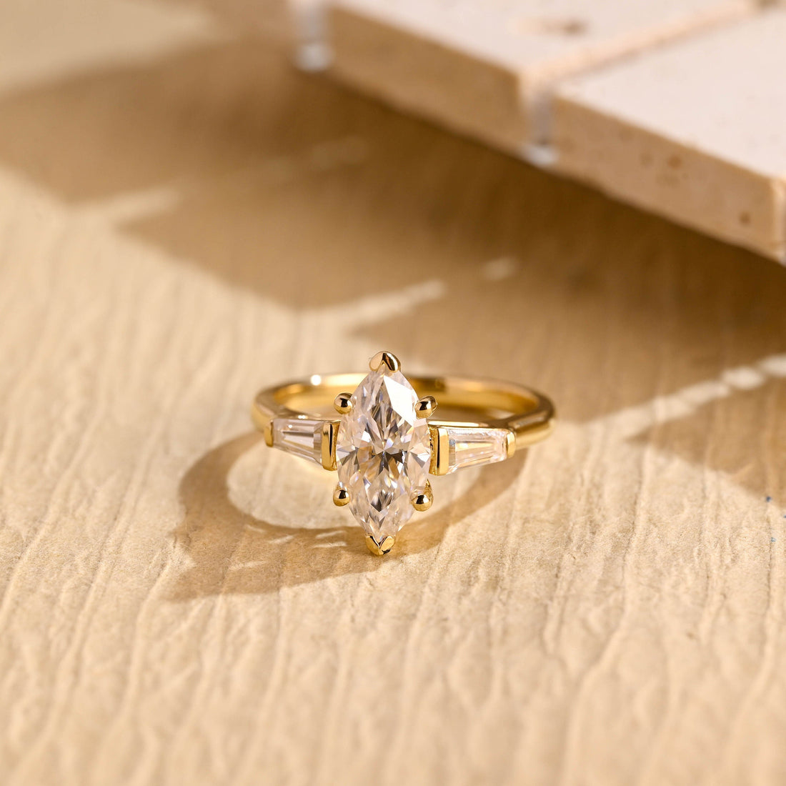 Marquise cut moissanite three stone engagement ring with tapered baguette side stones on a plain yellow gold band