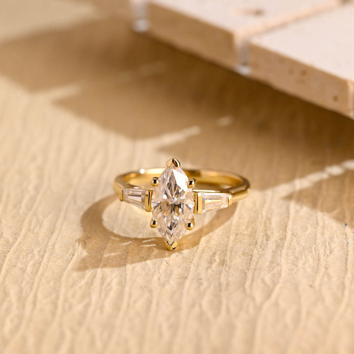Marquise cut moissanite three stone engagement ring with tapered baguette side stones on a plain yellow gold band