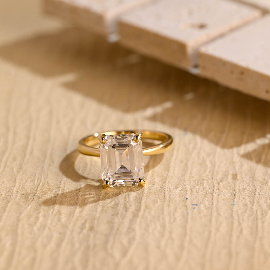 Emerald cut moissanite four claw solitaire engagement ring on a plain polished yellow gold band
