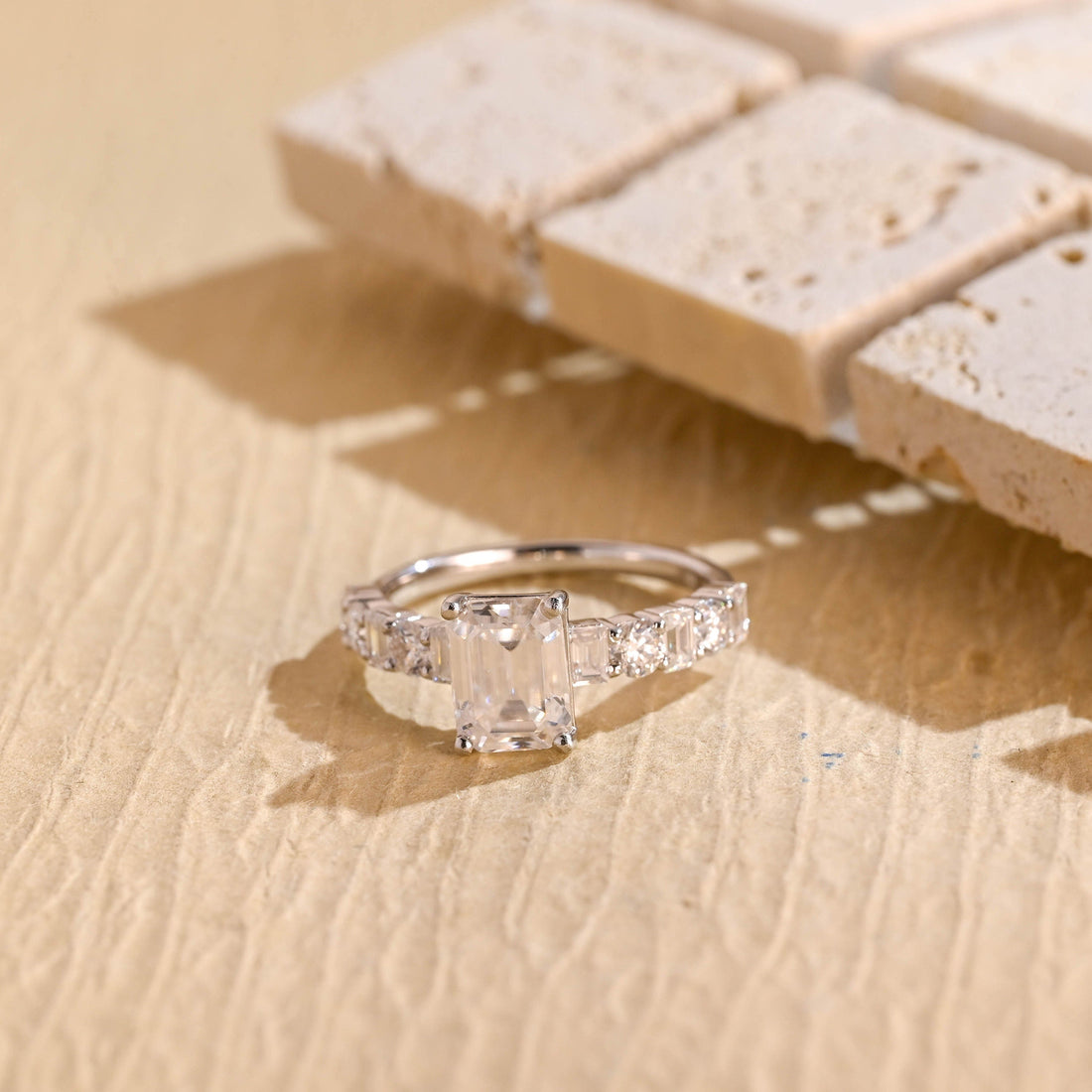 Emerald cut moissanite engagement ring on a white gold band set with alternating round and emerald cut stones