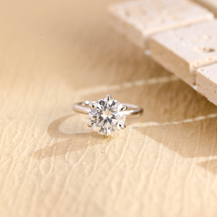 Round moissanite bridal solitaire engagement ring held by six rounded droplet shaped claws on a thin polished white gold band