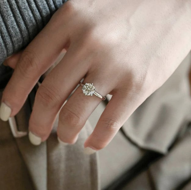 Round moissanite bridal solitaire engagement ring held by six rounded droplet shaped claws on a thin polished white gold band, view 2