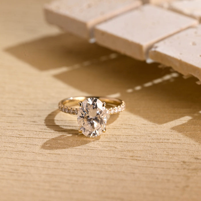 Large oval moissanite engagement ring with four claws and a scallop set pave round stone band in yellow gold