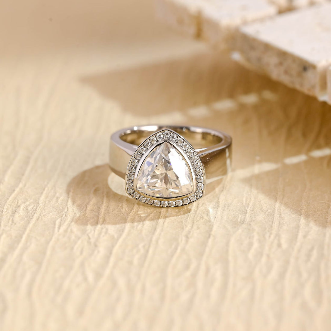 Trillion cut moissanite bezel halo engagement ring on a wide polished white gold band