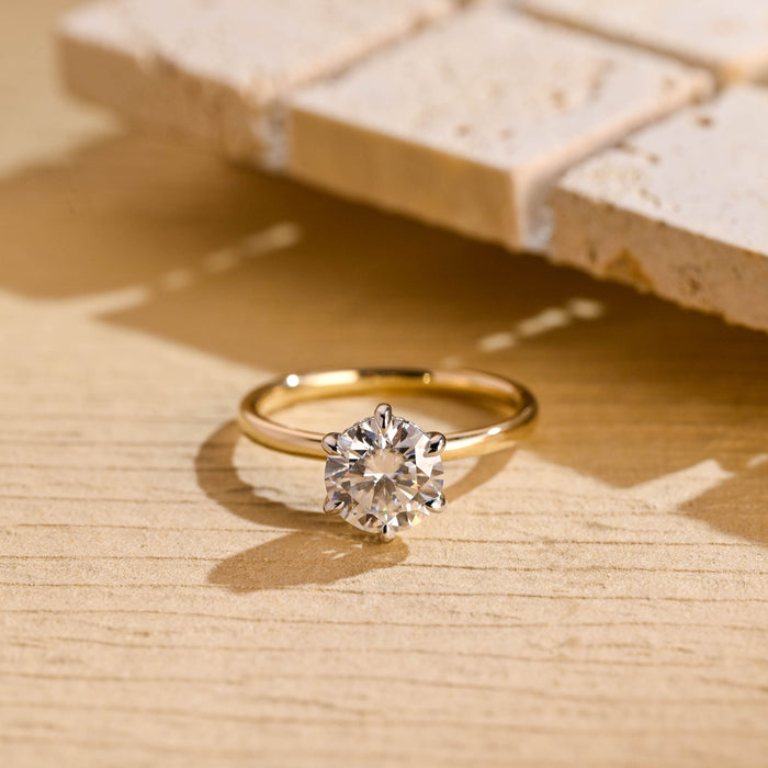 Round moissanite hidden halo engagement ring in six white claws on a slim polished yellow gold band