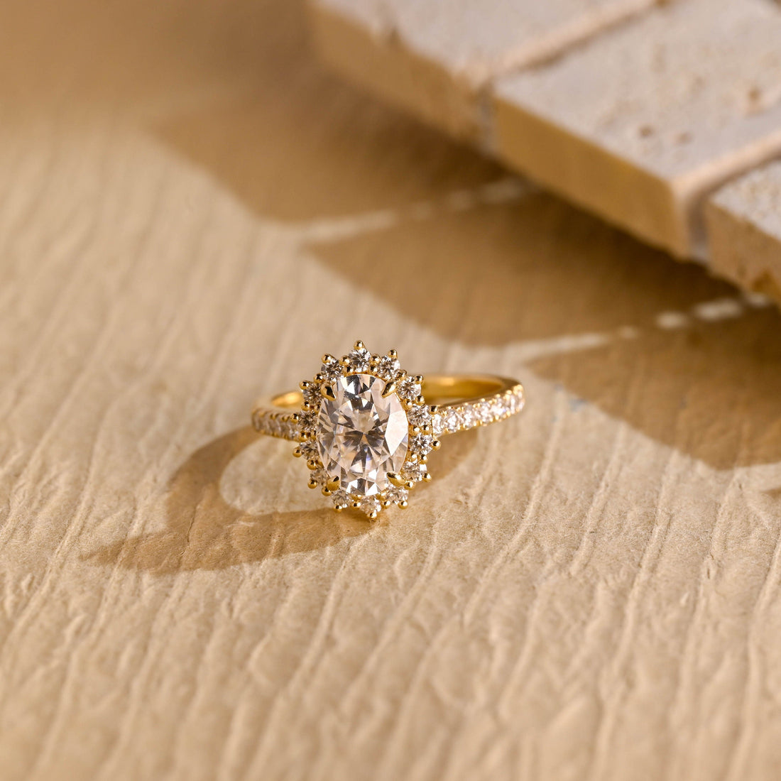Oval moissanite sunburst halo engagement ring with pointed prong tips around the halo and a pave set yellow gold band
