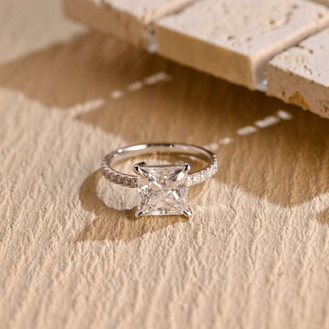 Princess cut moissanite four claw solitaire engagement ring on a pave set white gold band