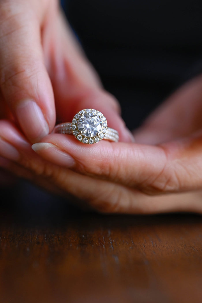 Round moissanite halo engagement ring with four claws and a wide yellow gold band pave set with three rows of small round stones, view 2