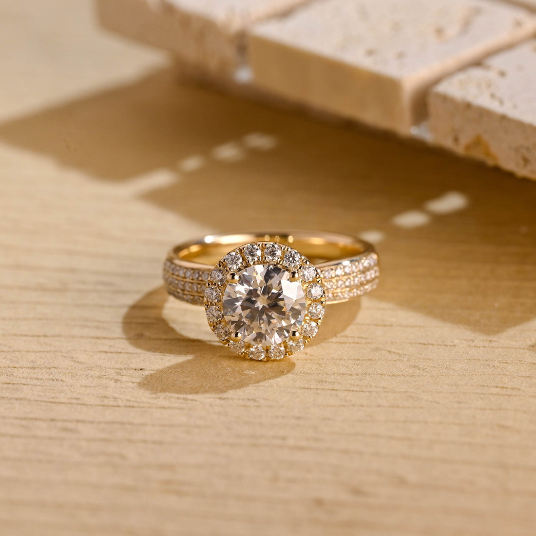 Round moissanite halo engagement ring with four claws and a wide yellow gold band pave set with three rows of small round stones