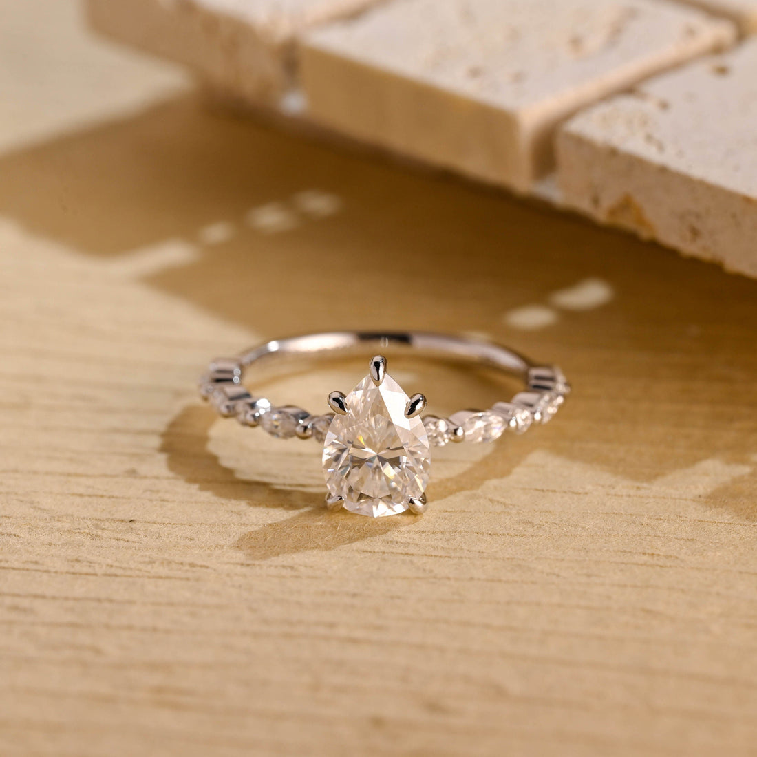 Pear cut moissanite engagement ring in claws on a slim white gold band set with alternating marquise and round stones
