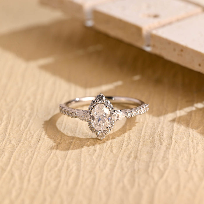 Oval moissanite vintage style halo engagement ring with a pointed halo, a pear shaped stone on each side and a pave set white gold band