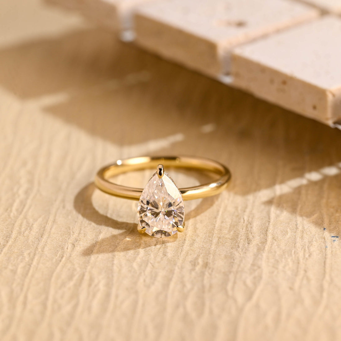 Pear cut moissanite hidden halo engagement ring in a three claw setting on a slim plain polished yellow gold band