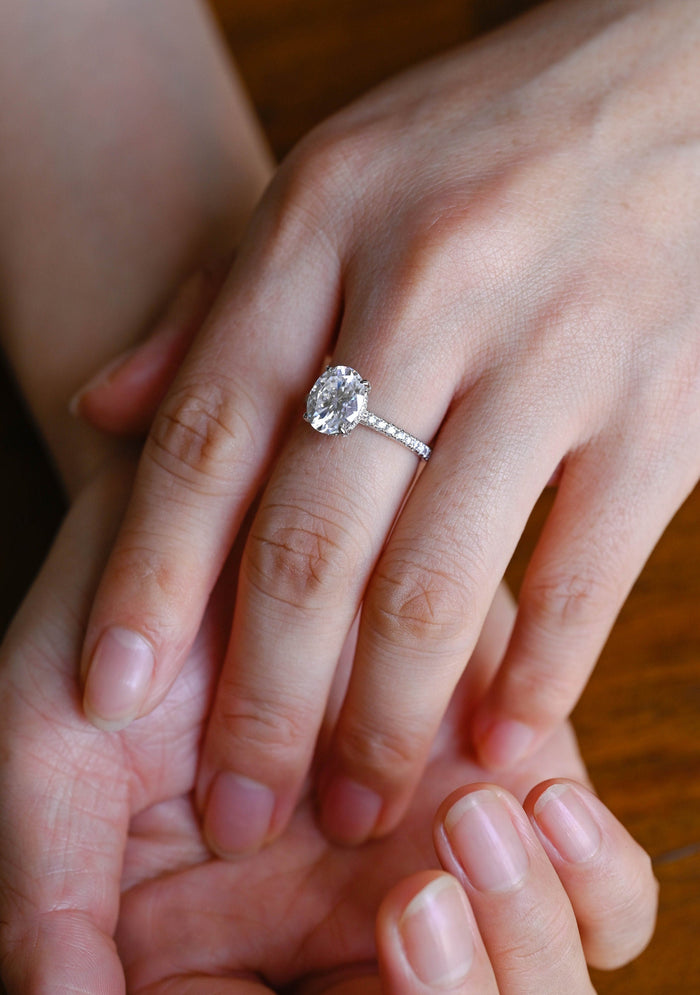 Oval moissanite hidden halo solitaire engagement ring with four claws and a slender white gold band set with fine round stones, view 2